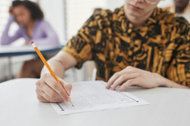 Young adult writing on exam paper in classroom setting, focus on pencil and paper.